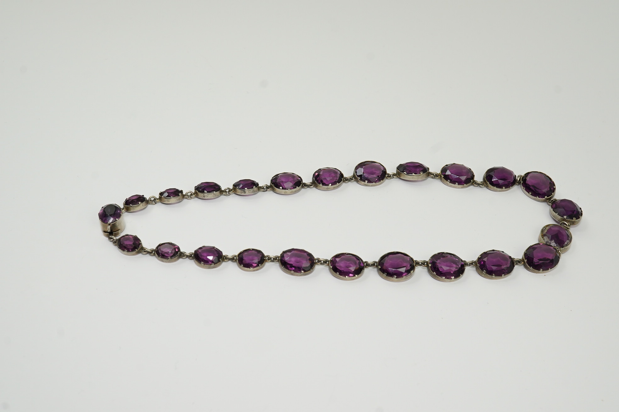 A Victorian silver and graduated oval cut amethyst paste set riviere necklace